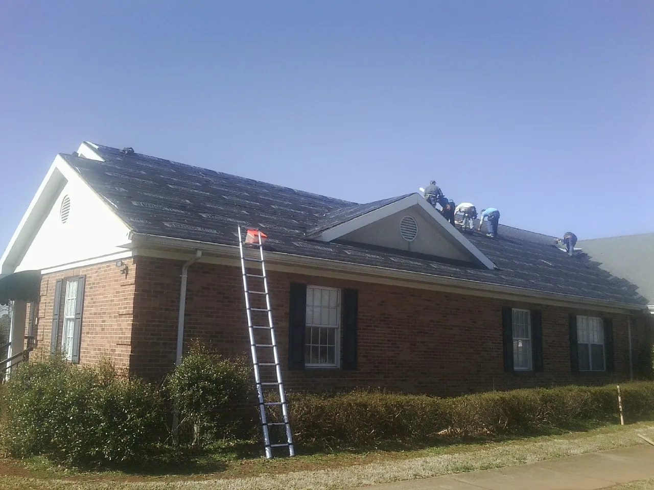 Crew tearing shingles off a brick ranch roof with a ladder set — Metal Roof Repair work by our crew in Frazee