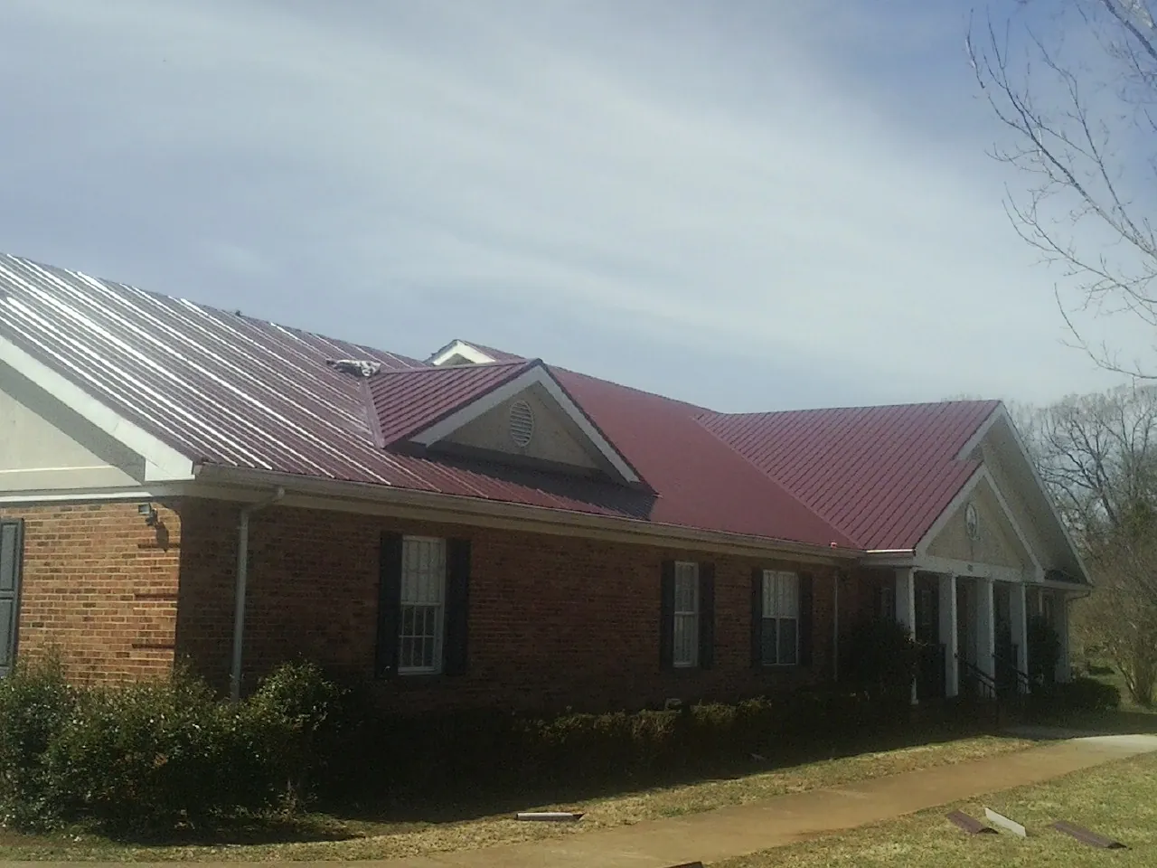 Red metal roof with gabled entries on a long brick building, from a Hail Damage Roof Repair job in Frazee