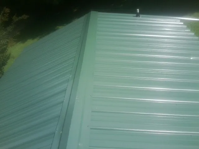 New green metal panels meeting at the ridge of a roof — Flat Roof Repair work by our crew in Frazee