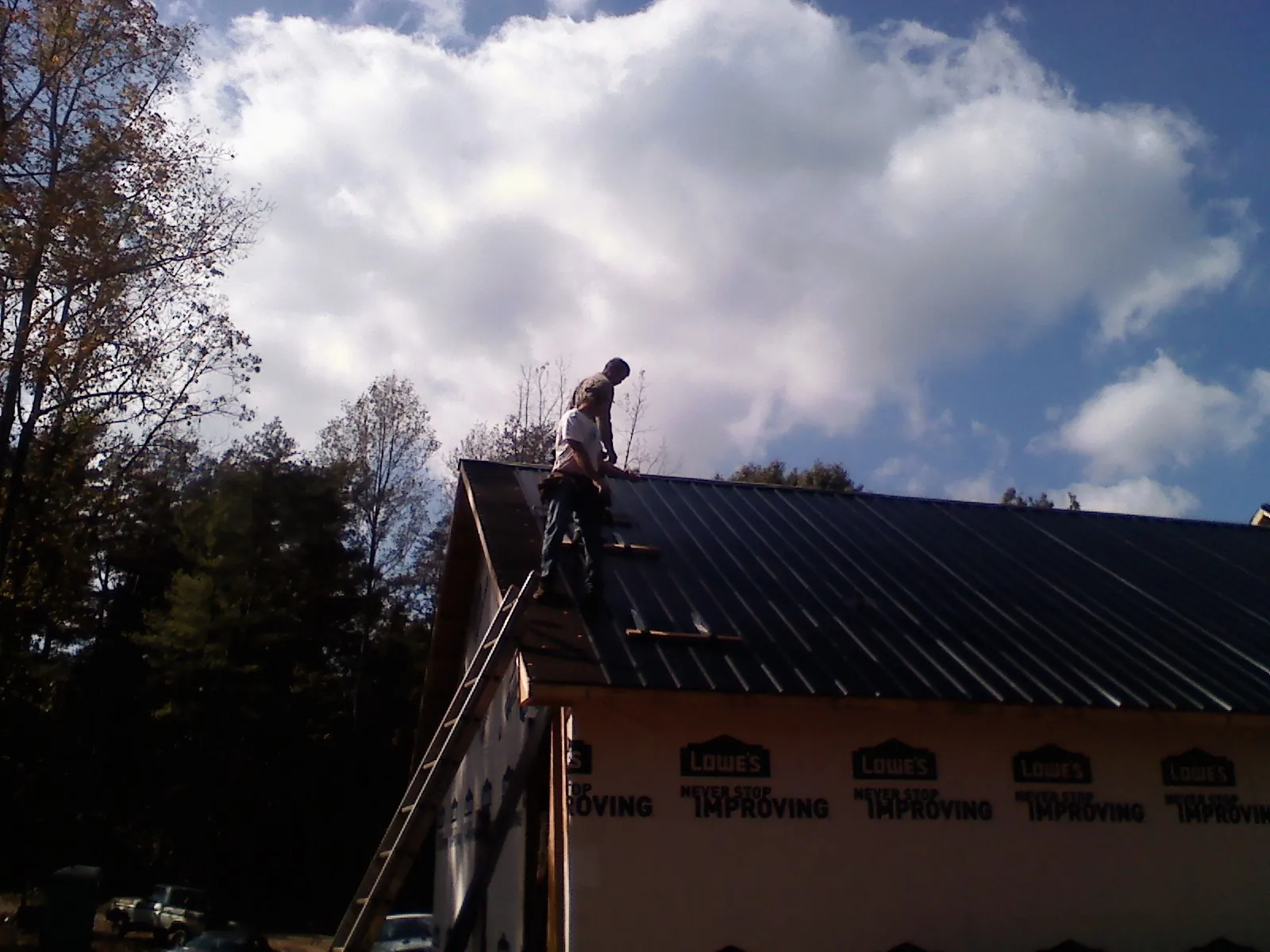 Roofer fastening dark metal panels high against a cloudy sky, from a Roof Inspection job in Frazee
