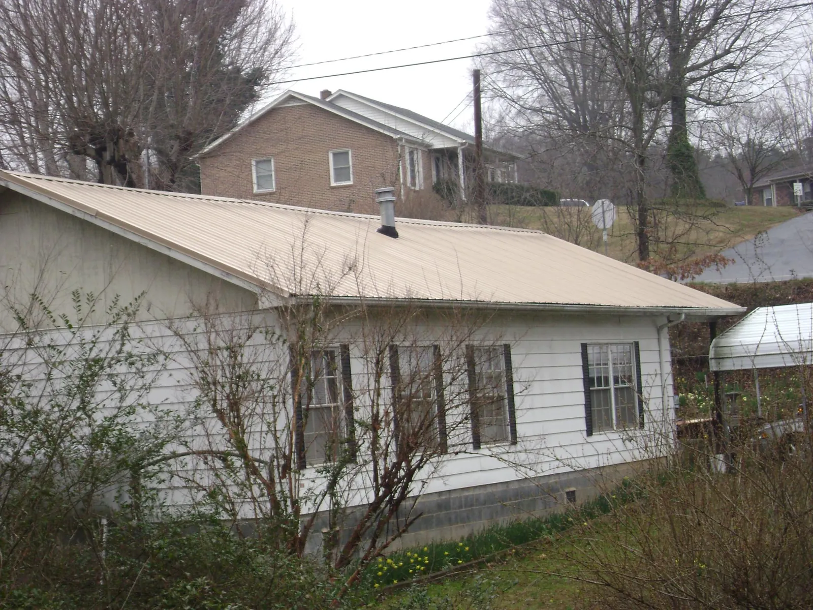 Tan metal roof on a white sided house set into a hillside — Commercial Roofing by Roofing Brothers in Frazee