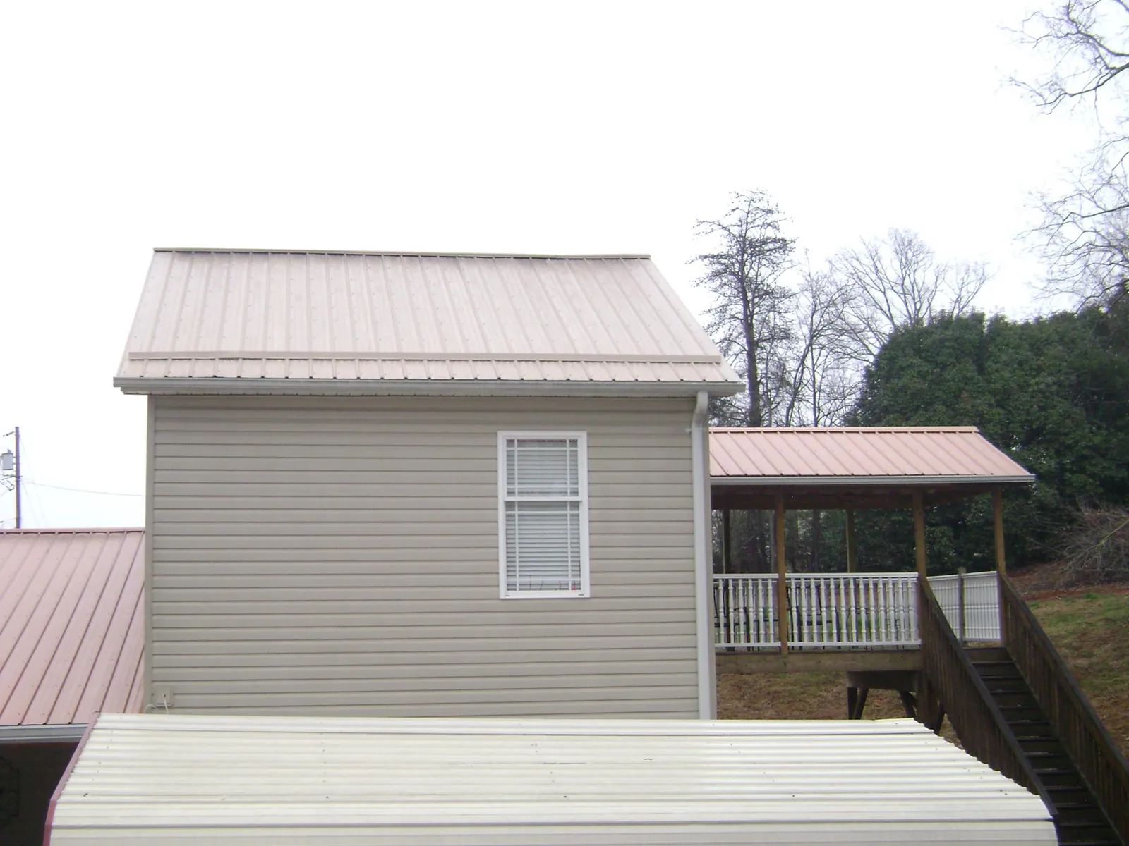 Tan metal roofs on a two story addition and attached porch, from a Roof Replacement job in Frazee